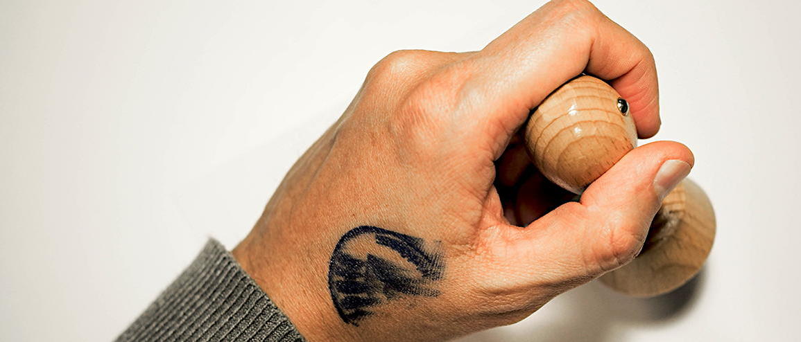 Stempelabdruck auf einer Hand, die einen runden Holzstempel hält.